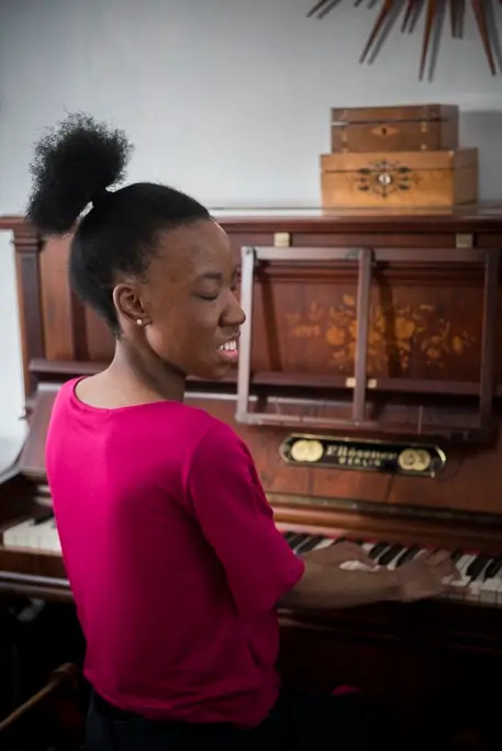 Blind psychotherapeutic counsellor, Sandra, playing piano in a pink t-shirt as a form of expressive therapy